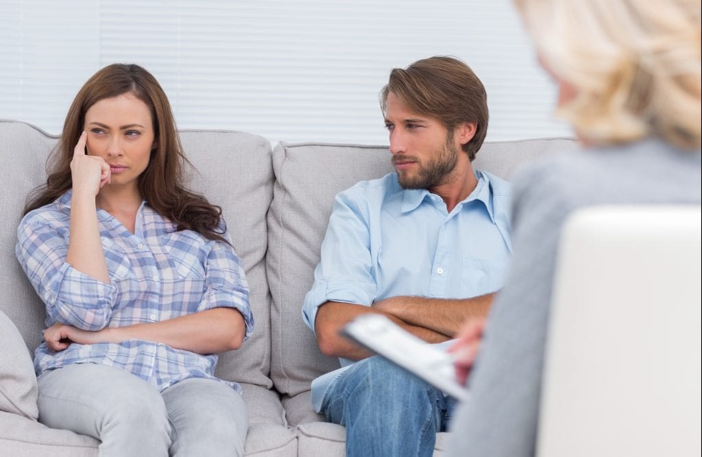 Troubled couple sit with arms folded in the office of the therapist